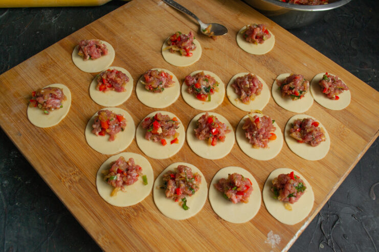 Portioning the filling onto dough circles Small portions of meat filling placed on cut-out dough circles
