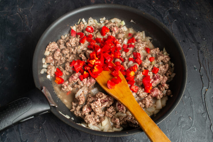 Folding in the bell pepper Diced red bell pepper mixed into the browned ground beef.