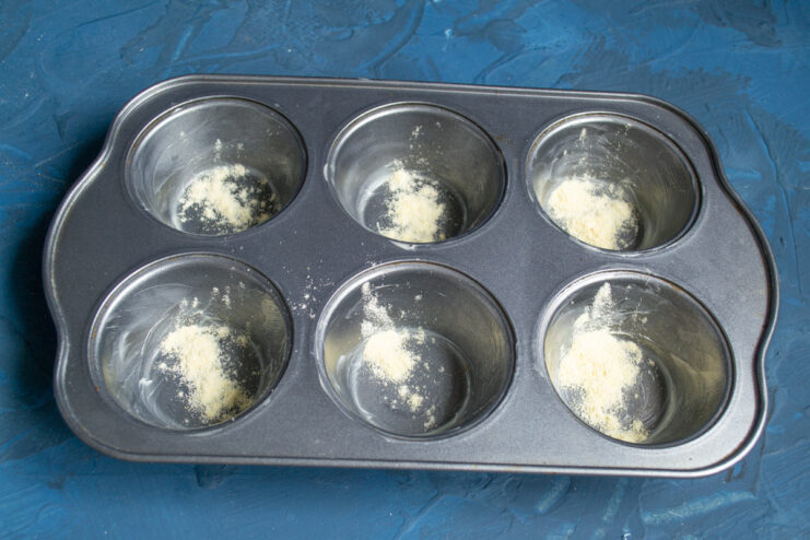 Adding cornmeal Cornmeal sprinkled inside greased muffin tin cavities.