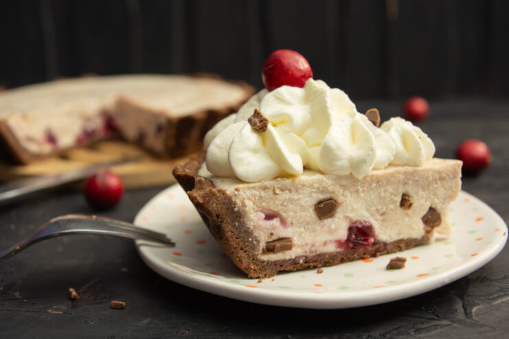 A slice of farmers cheese cheesecake on a plate garnished with whipped cream and a fresh berry