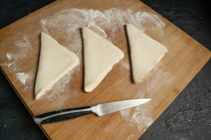 Puff pastry squares folded into triangles on a wooden surface