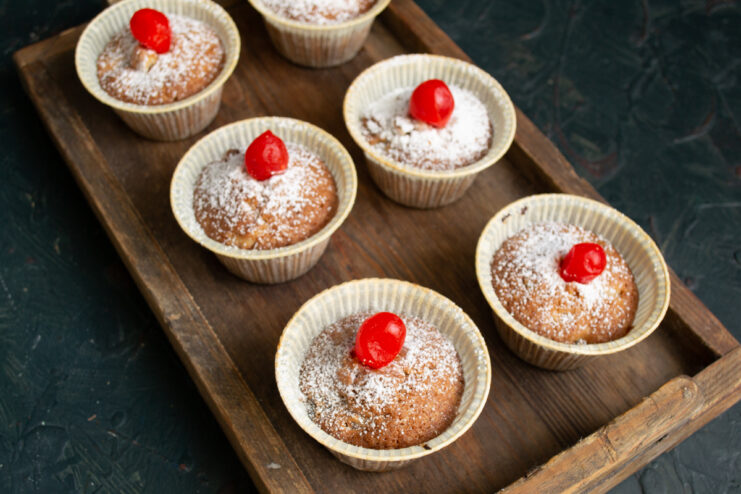 Decorating the muffins Muffins elegantly garnished with powdered sugar and candied kumquats on a wooden tray.