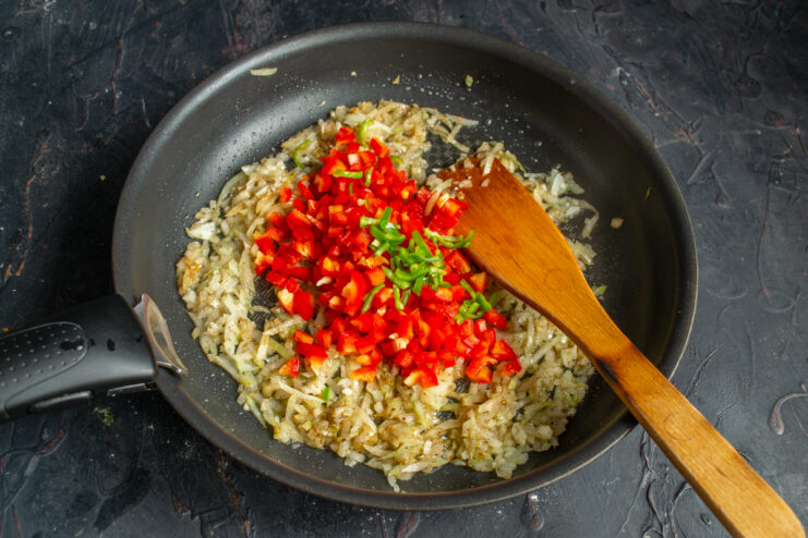 Adding bell pepper for juiciness and color Finely diced red and green peppers cooking with onions in a skillet