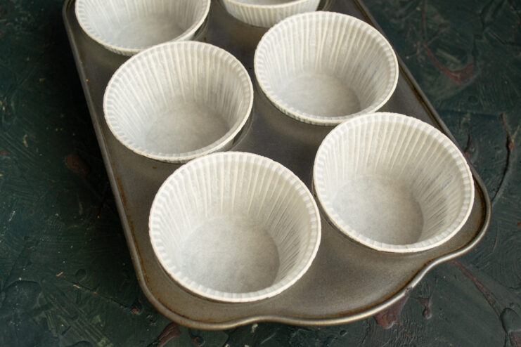 Preparing the muffin tin Metal baking tin lined with white paper muffin cups.