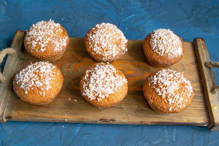 Garnished baked goods Almond muffins topped with desiccated coconut on a wooden board.