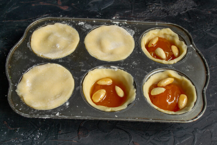 Placing smaller dough circles on top of the jam filling to seal the tartlets.