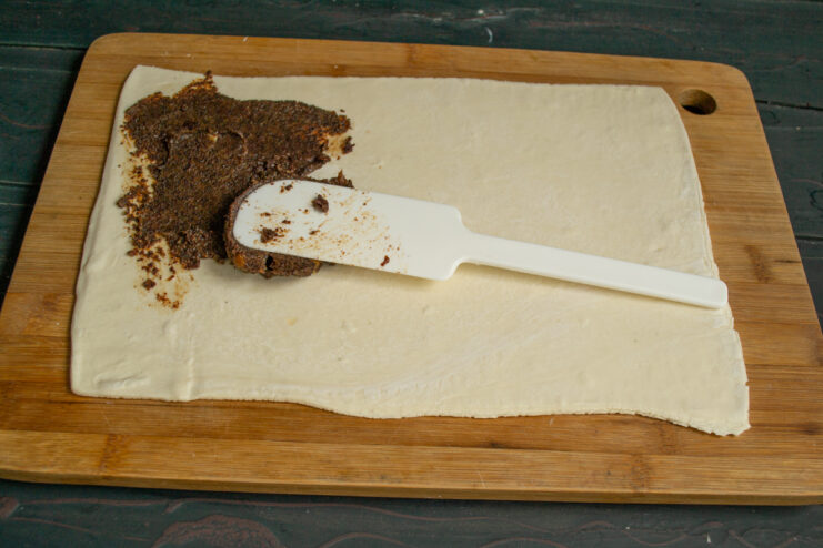 Adding the filling Spreading poppy seed filling onto rolled-out dough using a spatula.