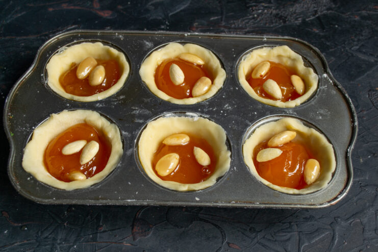 Filling the pastry shells with apricot jam and whole blanched almonds.
