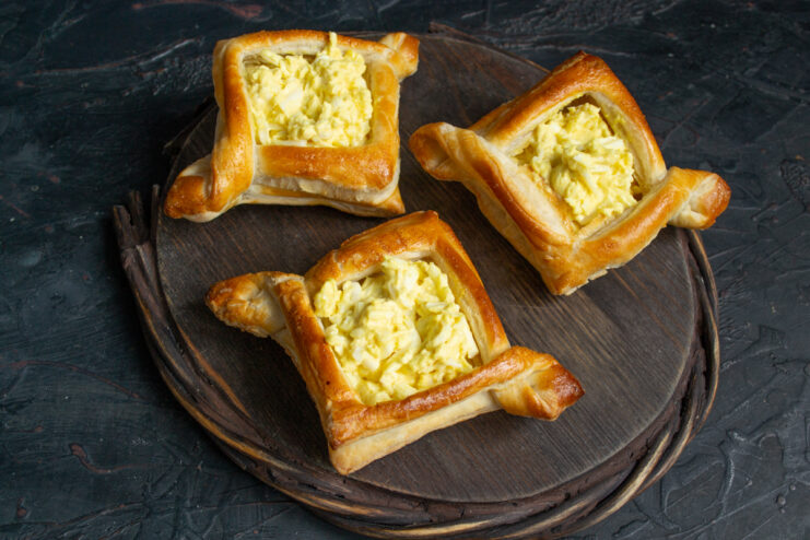 Baked puff pastry shells generously filled with egg salad on a wooden board