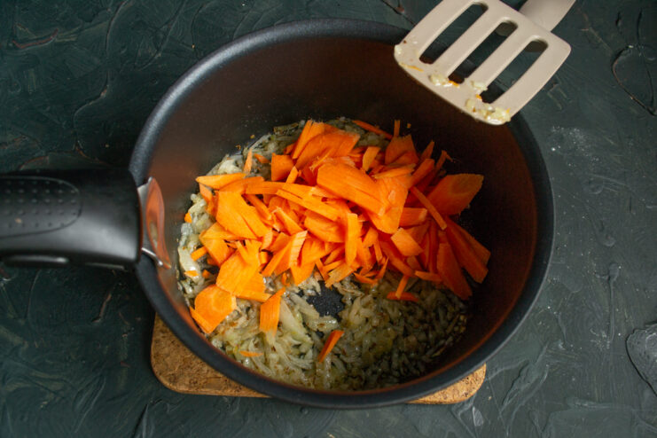 Adding the Carrots Thinly sliced carrots added to sauteed onions in a cooking pot.