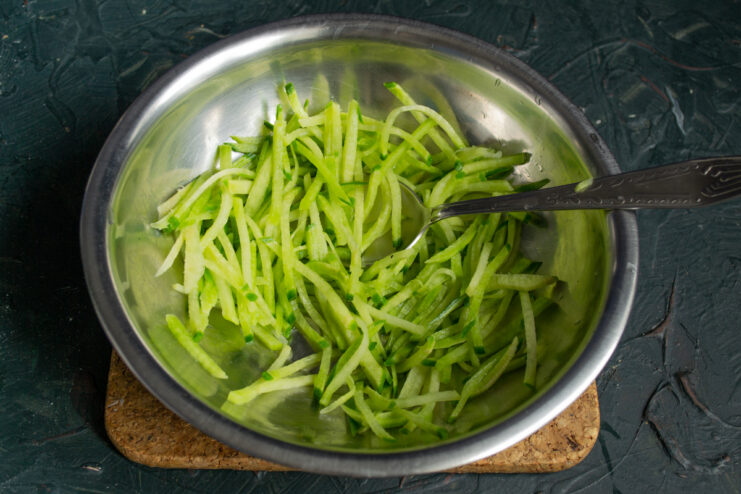 Julienned green radish in a metal bowl being prepped with salt