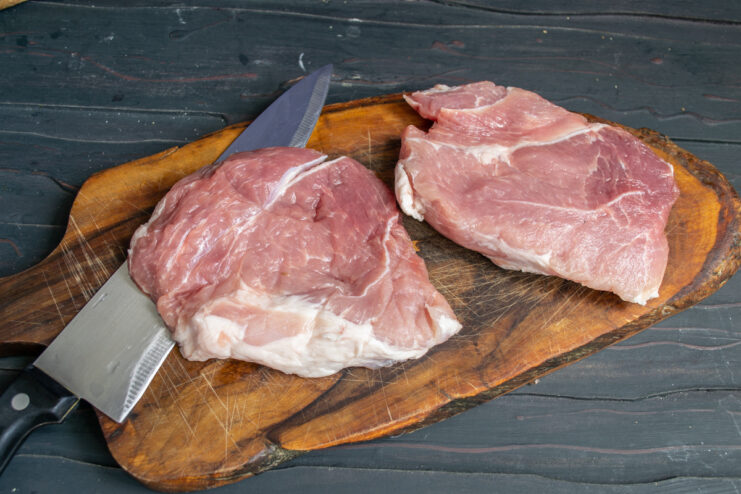 Prepping the Pork for Grilling Sliced raw pork pieces on a wooden cutting board.