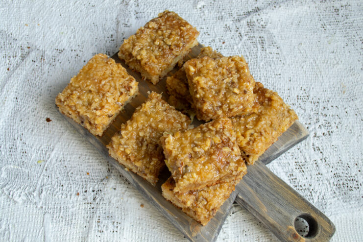 Slicing the cooled dessert Sliced walnut and coconut cake bars on a wooden serving board