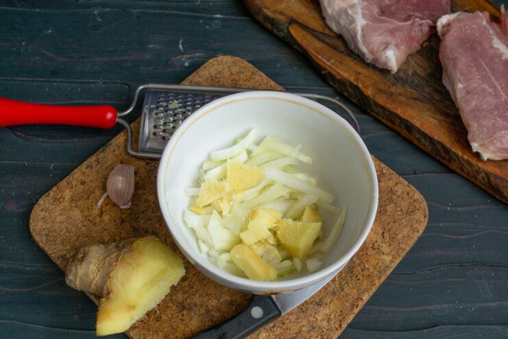 Korean Marinade Ingredients Chopped onion and fresh ginger root in a white bowl.