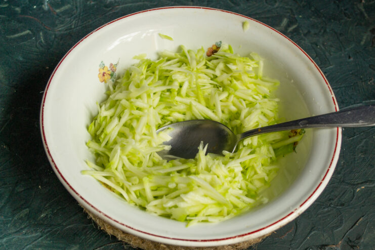 Grating The Zucchini Shredded zucchini flesh sitting in a white bowl