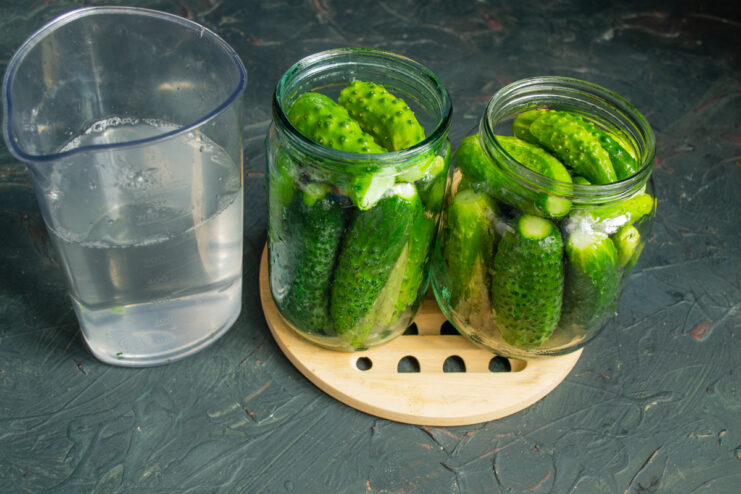 Packing cucumbers and measuring water Cucumbers packed tightly in glass jars next to a measuring cup filled with water