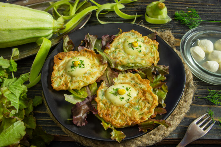 Plate of zucchini fritters with melted mozzarella and corn kernels on top