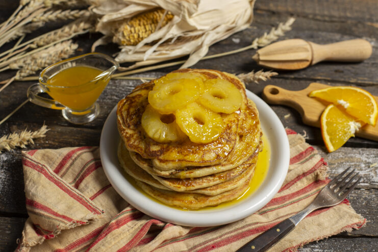Stack of whole wheat and cornmeal pancakes topped with orange syrup and pineapple