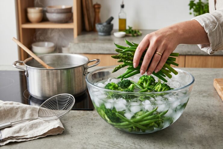 Submerging green asparagus into a bowl of cold water with ice cubes