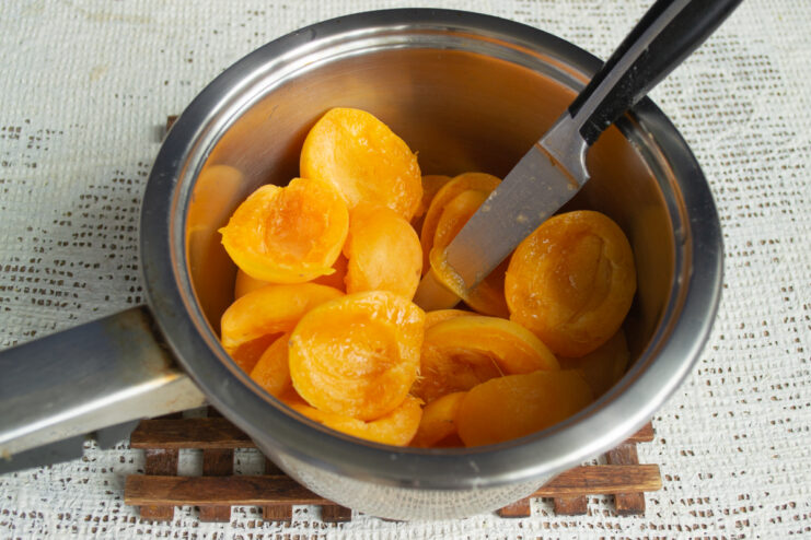 Halving and pitting the fruit Fresh apricot halves placed inside a heavy-bottomed saucepan.