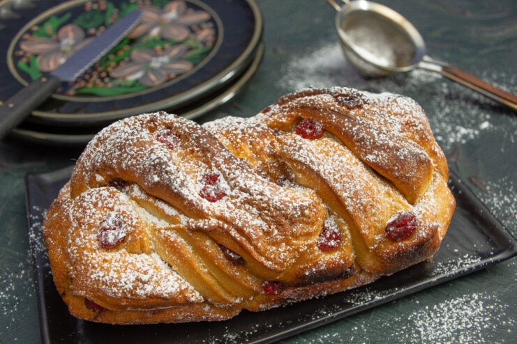 Baked Polish babka dusted with powdered sugar showing cherry filling on a dark background