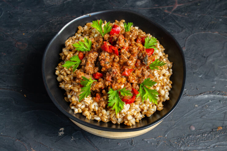 Serving the finished dish A portion of spelt topped with rich meat sauce in a deep black bowl.