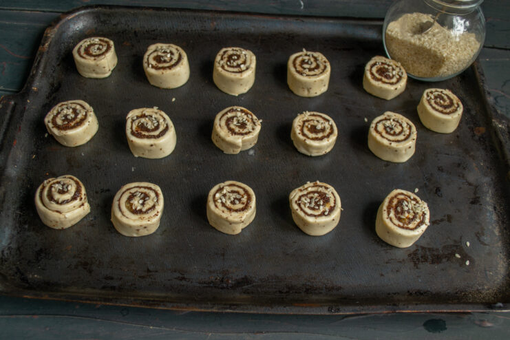 Garnishing the pinwheels Sprinkling sesame seeds over raw egg-washed pastry pinwheels.