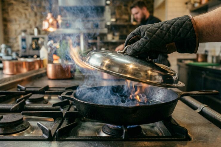 Safe extinguishing of burning cooking oil Chef covering a burning skillet with a metal lid to safely extinguish an oil fire on the stove.
