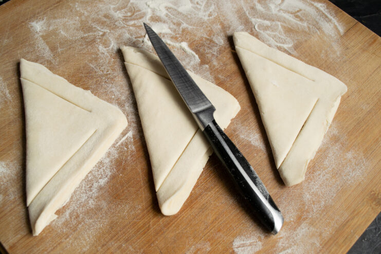 Making cuts along the edges of folded triangular puff pastry dough