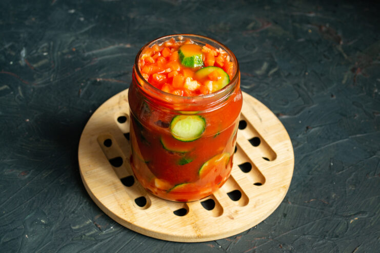 Pouring boiling tomato juice over cucumbers and peppers in a glass jar