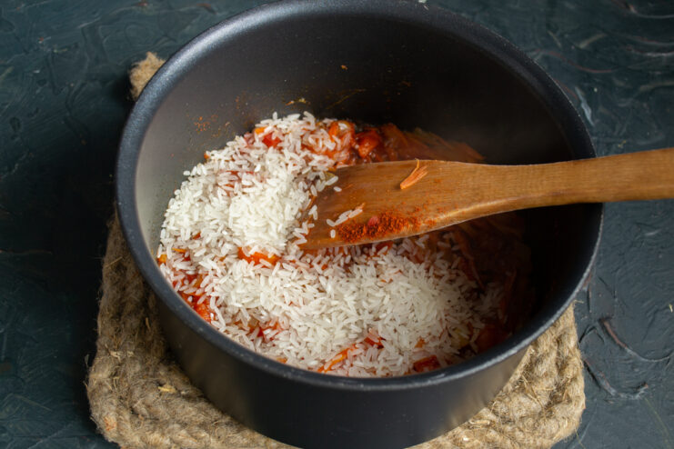 Toasting rice with vegetables Washed rice poured into the vegetable base in the pot.