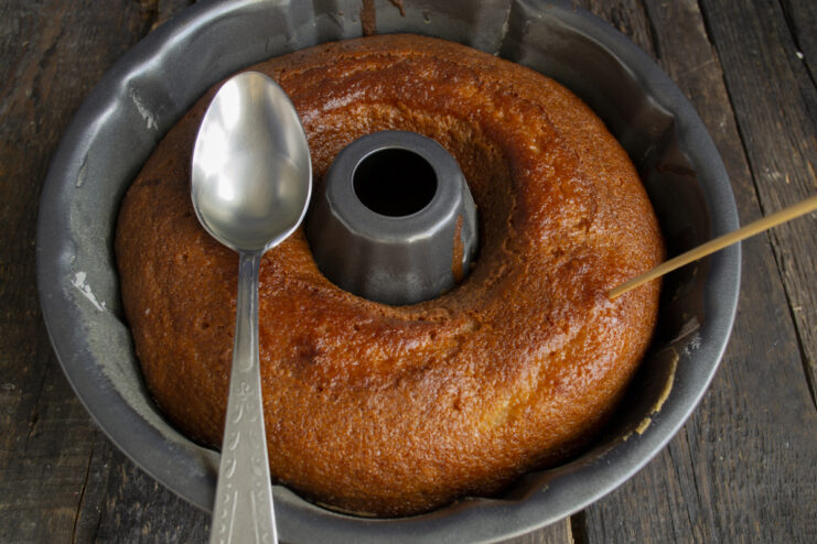 Soaking the Cake in Syrup Drizzling pineapple syrup over a hot baked cake in a pan