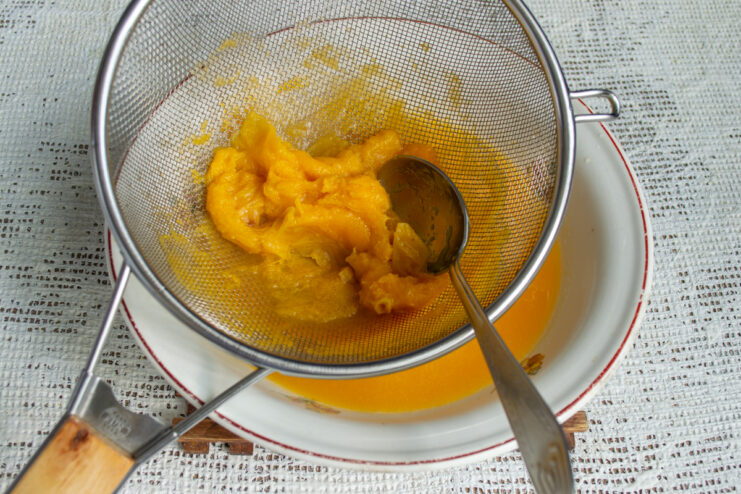 Passing through a fine sieve Pushing hot apricot mixture through a fine mesh sieve with a spoon.