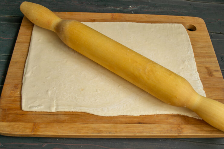Rolling out the dough Rolling out a sheet of puff pastry with a rolling pin on a wooden board.