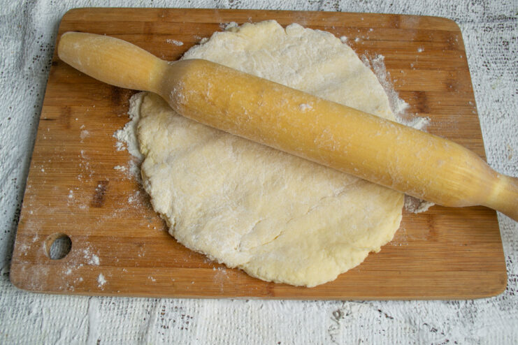 Rolling Out the Dough Rolling out dough with a wooden rolling pin on a cutting board.