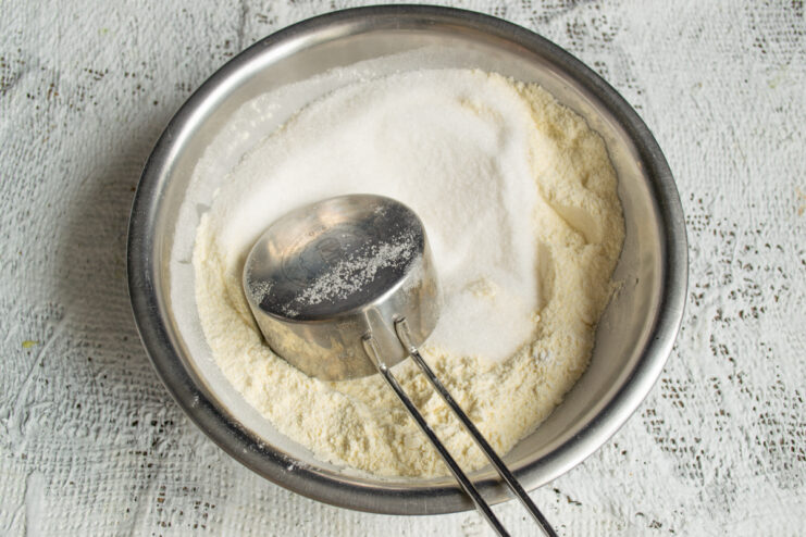 Combining Dry Ingredients Adding granulated sugar to the dry flour mixture in a bowl.