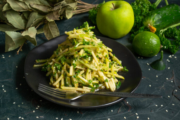 Vibrant green radish, apple, and cucumber salad served on a black plate