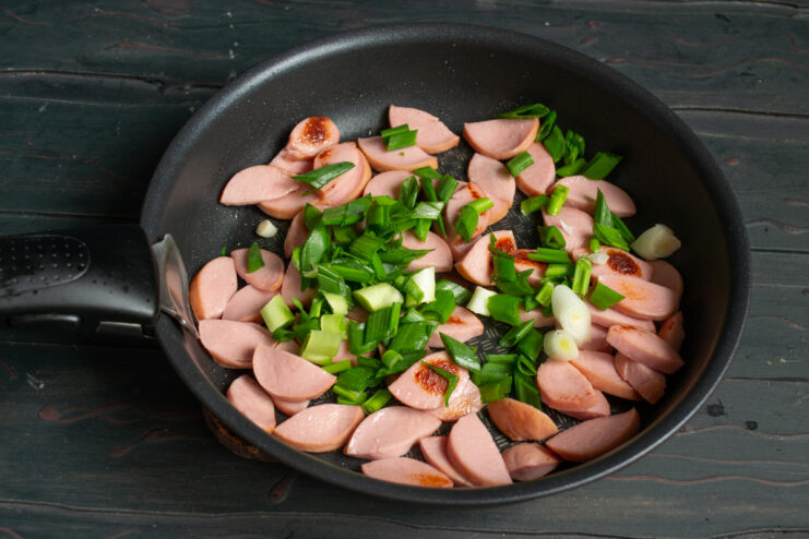 Sausages With Onions Sausages cooking with chopped green onions in a pan