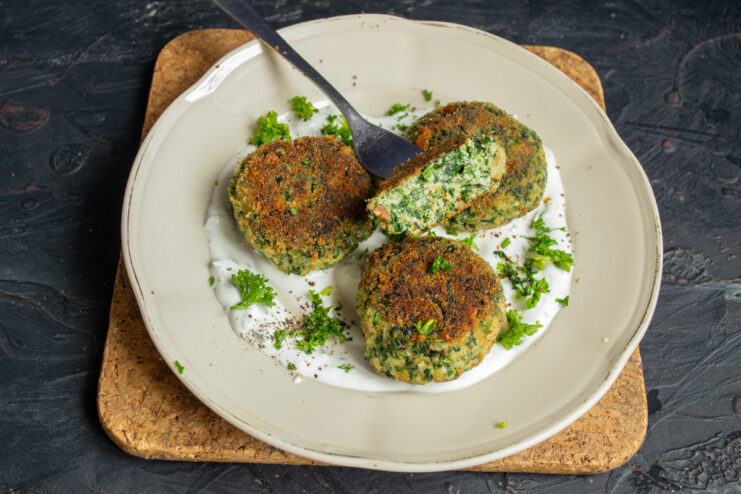 Hot spinach patties plated with white creamy sauce and fresh parsley