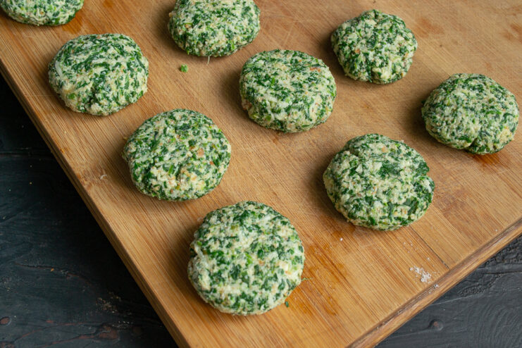 Formed round spinach patties resting on a wooden cutting board