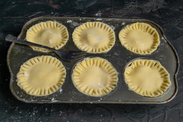 Crimping the edges of the raw tartlets with a fork inside the muffin tin.