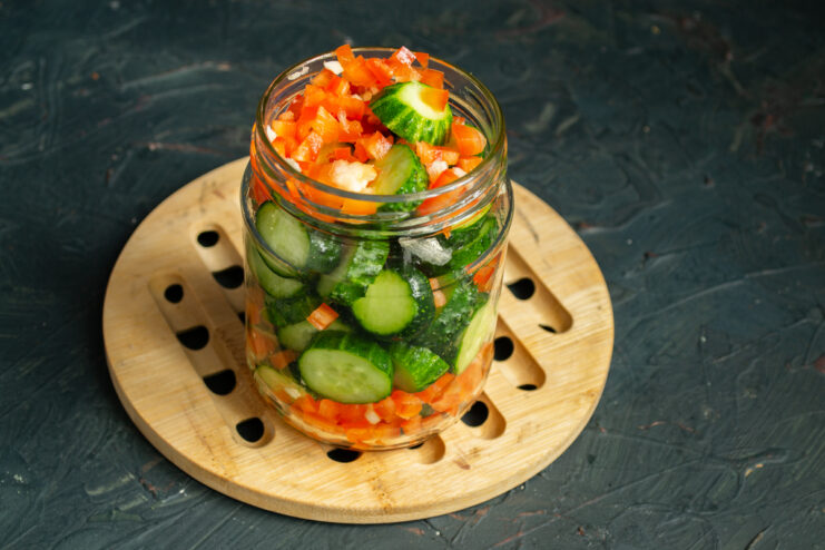 Diced red sweet bell pepper and minced garlic layered over sliced cucumbers in a jar