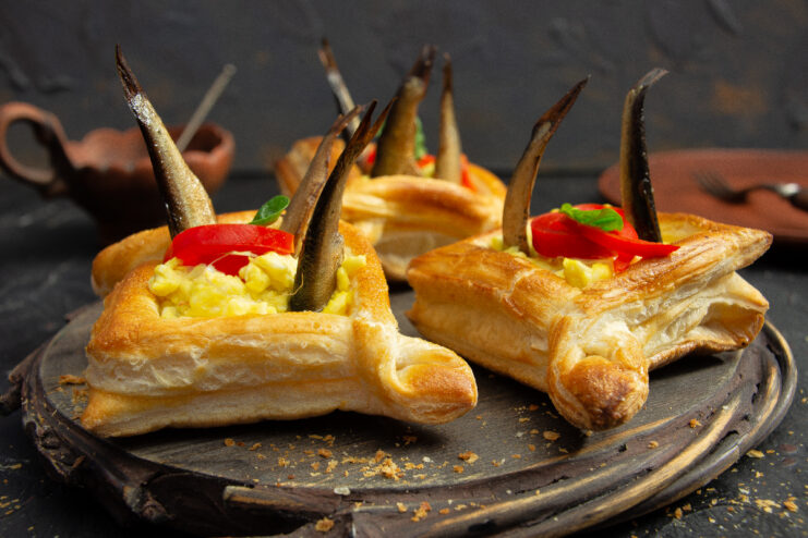 Puff pastry tarts with egg salad and sprats garnished with red bell pepper strips and fresh herbs