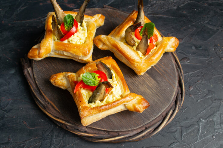 Finished puff pastry tart topped with three sprats, red pepper, and fresh herbs
