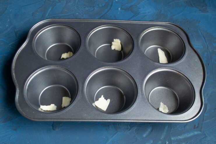 Preparing the muffin tin Greasing muffin tin cavities with pieces of softened butter.