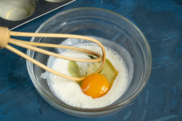 Wet ingredients base Whisking yogurt and a cracked egg in a glass mixing bowl.