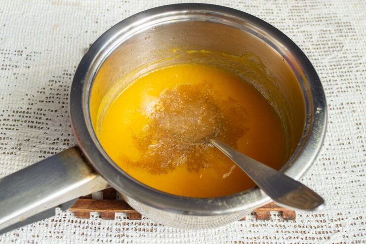 Incorporating the gelatin Mixing bloomed gelatin into hot vibrant apricot puree in a pot.