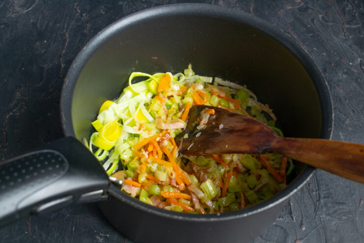 Adding the bacon and vegetable mixture to the leeks Mixing sautéed vegetables and bacon with leeks in a cooking pot