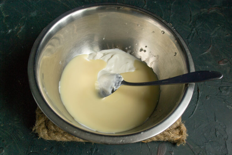 Mixing the cream base Mixing sour cream and sweetened condensed milk in a deep glass bowl
