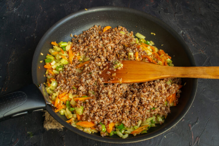 Mixing the buckwheat and vegetable filling Mixing cooked buckwheat with sautéed vegetables in a pan